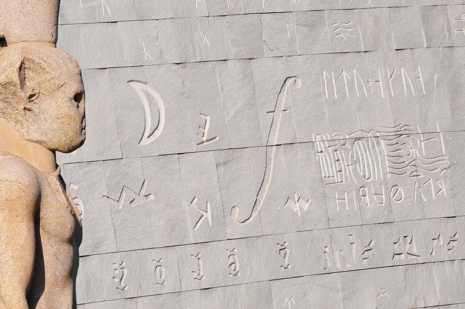 The beautiful exterior of the Alexandria Library in Alexandria, Egypt. The focus is on the ancient statue on the left; the background is the building exterior, engraved with characters and symbols.